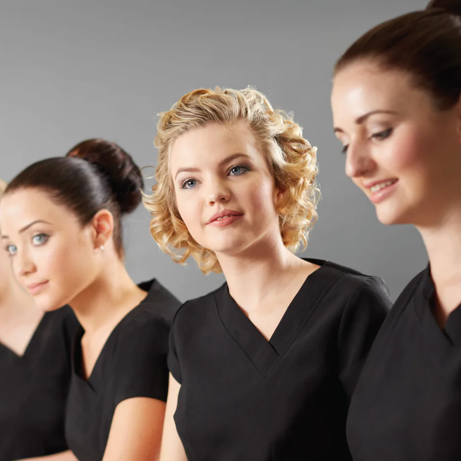 Three women in black professional uniforms standing against a gray background. The center woman has blonde curled hair, while the women on either side have different hairstyles, showcasing various ...